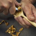 A Craftsman Carving Wood, Shaping The Bowl Of A Handcarved Wooden Spoon With A Sharp Handheld Tool.